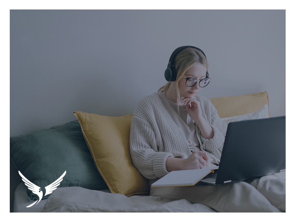 Woman writing in a notebook, whilst on her laptop.